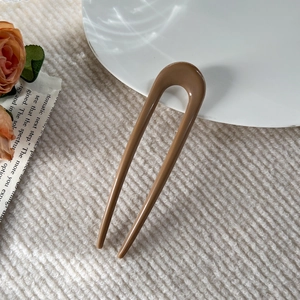 Macro shot of an elegant amber U-shaped hair pin on a white ceramic plate with a rose