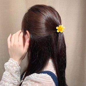 Tropical yellow plumeria flower hair claw clip worn by a model for a summer vacation look