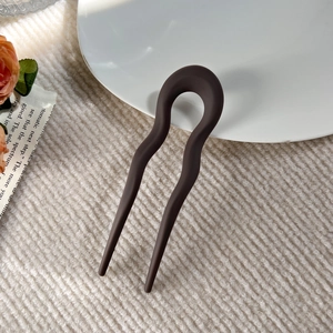 Detail of matte brown U-shaped hair pin with wave design on a white ceramic plate