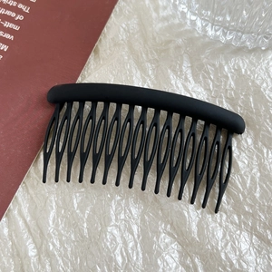 Close-up of matte black 15-tooth hair comb clip on a textured beige background
