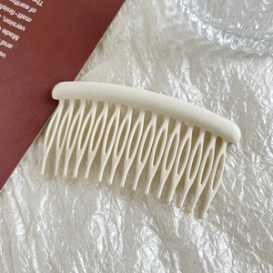 Detail of a creamy white matte 15-tooth hair comb on a minimalist textured background