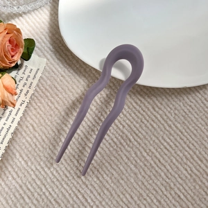 Detail of a purple matte wavy U-shaped hair pin for buns placed on a ceramic plate