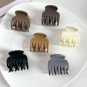 Détail de 6 petites pinces à cheveux mates aux tons Morandi sur une assiette en céramique