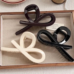 Close-up of three minimalist hollow half-moon hair claws in brown, black, and cream colors