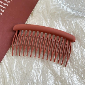 Detail view of brick red matte hair comb with hollow 15-tooth design on a textured background