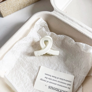 Primer plano de pinza de pelo de flor beige mate sobre papel blanco en una caja