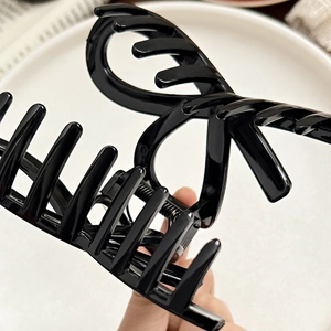 Detail of glossy black bow hair claw clip showing the sturdy metal spring mechanism