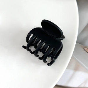 Détail d'une petite pince à cheveux noire mate avec 7 dents sur un socle blanc