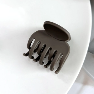 Détail d'une grande pince à cheveux marron foncé mate avec design à dents croisées sur blanc