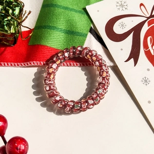 Close-up of a festive red spiral hair tie featuring Santa, trees, and snowflake patterns