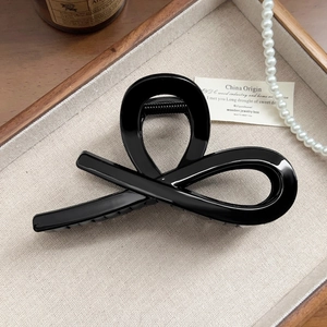 Detail of glossy black cross-loop hair claw clip on wooden tray with pearls