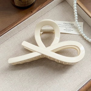 Detail of a creamy white hollow hair claw clip on a rustic wooden tray with pearls