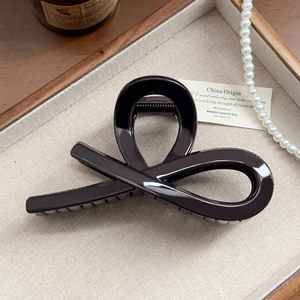 Detailed view of glossy dark brown hair claw clip on a rustic linen tray with pearls
