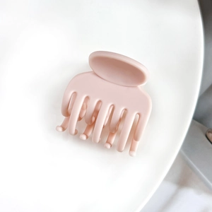 Détail d'une grande pince à cheveux rose mat avec des dents imbriquées sur fond blanc