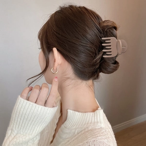 Pince à cheveux marron mat et créoles dorées portées par une femme en pull blanc