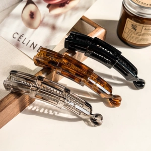 Three matte banana hair clips in amber, black, and grey with a durable metal spring