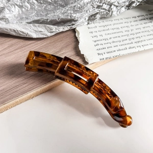 Close-up of tortoise shell pattern banana hair clip with amber resin texture on wood