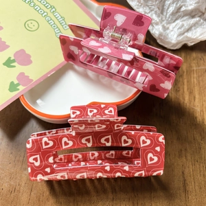 Detail of pink and red heart pattern hair claw clips with metal spring on a wooden table