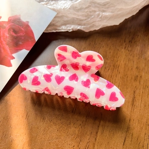 Macro shot of large pearl white claw clip featuring pink heart prints on a wood surface