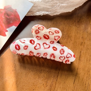 Close-up of white acetate hair claw clip with red heart and lip prints on wooden surface