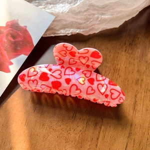 Detail showing pink hair claw clip with red heart patterns and translucent finish