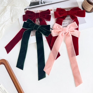 Close-up of four velvet bow hair clips in red, green, and pink colors on white background