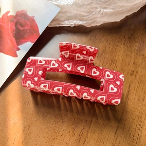 Rectangle red hair claw clip with white hearts and rose theme detail on wood surface