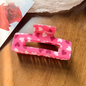 Detailed view of rose pink rectangular hair claw with heart patterns on wood background