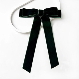 Close-up of deep green velvet bow hair clip with long ribbons on a white tray