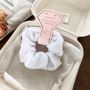 Close-up of white velvet scrunchie in a premium gift box with an elegant brand tag