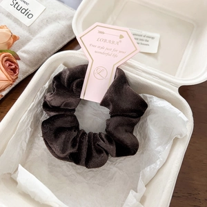 Detail of dark brown velvet scrunchie on branded card inside a gift box packaging