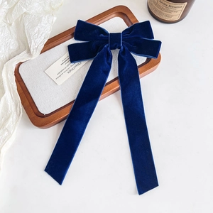 Detail of elegant dark blue velvet bow hair clip with long flowing ribbons on tray