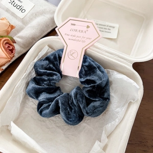 Macro detail of navy blue velvet scrunchie on brand card packaging in a gift box