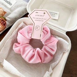 Close-up of pink velvet scrunchie displayed in gift packaging with branded card
