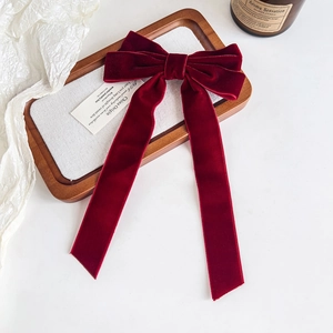 Detail view of a luxury burgundy velvet bow hair clip with long ribbons on a stylist tray
