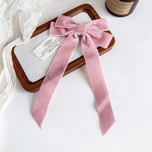Close-up of velvet rose pink bow hair clip with elegant long ribbons on a wood tray