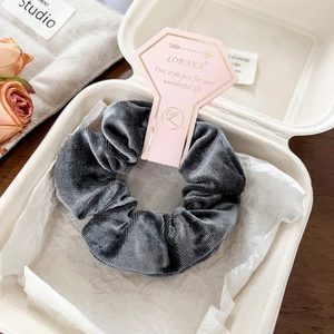 Macro shot of dark grey velvet scrunchie in premium cardboard display and white gift box