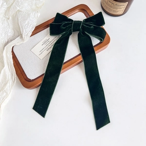 Detail shot of a dark green velvet bow hair clip on a wooden display tray with a candle