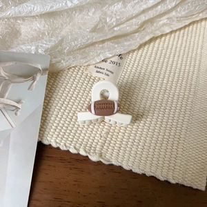 Détail d'une pince à cheveux mate crème avec un motif de football américain sur un tapis