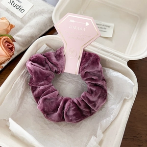 Close-up of purple velvet hair scrunchie with ribbed texture on hexagon display card