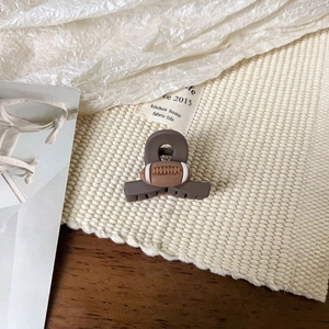 Gros plan d'une pince à cheveux rugby marron mat sur un tissu texturé de qualité