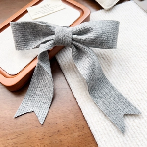 Détail d'une pince à cheveux avec nœud en tricot gris et ruban sur un plateau en bois