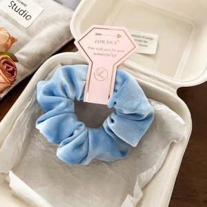 Close-up of a premium light blue velvet scrunchie in an elegant gift box with a pink tag