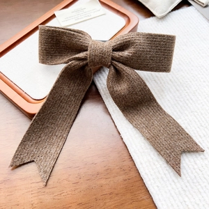 Détail d'une pince à cheveux nœud en tricot marron avec rubans sur un plateau en bois