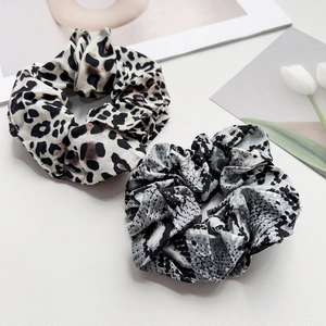 Detail shot of leopard and snake print satin hair scrunchies on a soft textured background