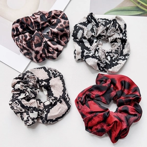 Close-up of four assorted leopard and snake print scrunchies with satin texture
