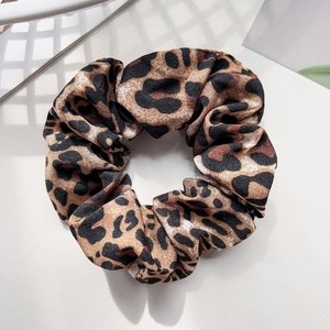 Detail of leopard print hair scrunchie made of silky chiffon fabric on a white background