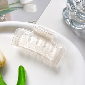 Détail d'une pince à cheveux mate crème ajourée posée sur une assiette décorative blanche