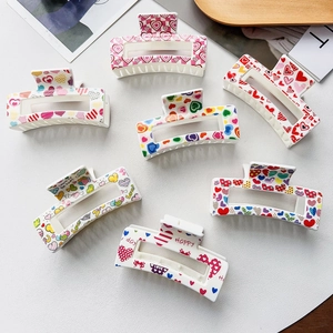 Close-up of white rectangular hair claws with colorful heart patterns and love slogans