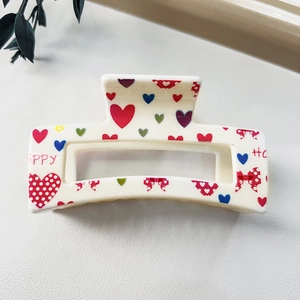 Detail of square hollow hair claw with colorful heart and bow prints on white glossy surface